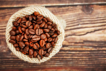 Freshly roasted aromatic coffee in a burlap bag on a wooden background.