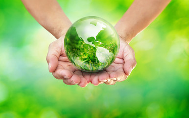Hands holding globe glass earth with green grass field in side on blurred light nature background,  World Environment Day and Save our Earth Concept