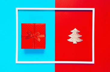 Christmas composition with present box and decorative fir tree on red and blue background with white frame. Winter holiday concept
