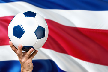 Costa Rica soccer concept. National team player hand holding soccer ball with country flag background. Copy space for text.