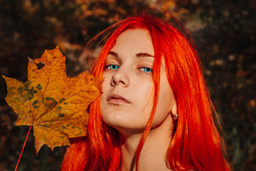 Sexy beautiful redhead girl with long, strong and thick hair. Perfect woman portrait on a background of autumn foliage. Gorgeous deep blue eyes. Natural beauty, clean skin, face and hair care.