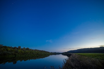 Blue sky over river, forest and meadow at sunset.