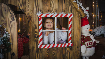 Funny little toddler girl peeping out the window playing with snow. Children play outside in the winter. Children have fun at Christmas. Children play building a snowman for Christmas. Photo studio