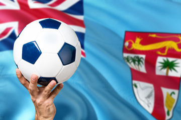 Fototapeta premium Fiji soccer concept. National team player hand holding soccer ball with country flag background. Copy space for text.