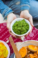 Green pesto paste dip in bowl. Hands holds pesto sauce.