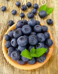 Bowl of fresh blueberries on rustic wooden old table. Freshly picked blueberries in bowl. Healthy organic fruit background. Organic food raw blueberries and mint leaf for healthy lifestyle.