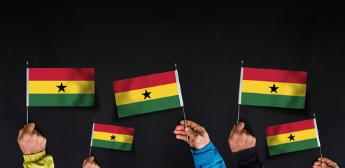 Fototapeta na wymiar Hands holds flags of Ghana on dark background