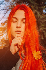 Sexy beautiful redhead girl with long, strong and thick hair. Perfect woman portrait on a background of autumn foliage. Gorgeous deep blue eyes. Natural beauty, clean skin, face and hair care.