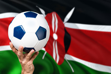 Fototapeta premium Kenya soccer concept. National team player hand holding soccer ball with country flag background. Copy space for text.