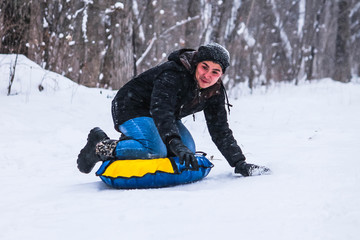 Cheerful guy rolls down the hill on snow tubing in the woods . Sledding. Winter entertainment.