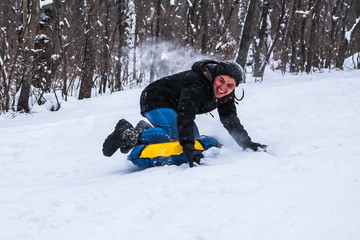 Fototapeta na wymiar Cheerful guy rolls down the hill on snow tubing in the woods . Sledding. Winter entertainment