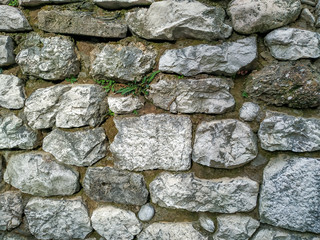 Rock stone wall background made of bricks on a wall of the building in the outdoors with rough texture and interesting natural pattern with grass and other plants