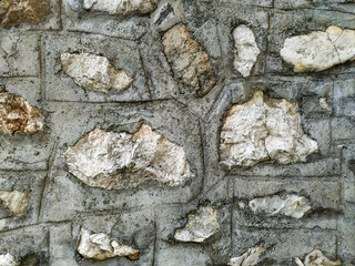 Rock stone wall background made of bricks on a wall of the building in the outdoors with rough texture and interesting natural pattern with a lot of cement around