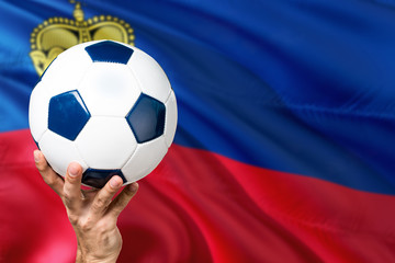 Naklejka premium Liechtenstein soccer concept. National team player hand holding soccer ball with country flag background. Copy space for text.