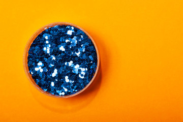 Jar with trendy blue sparkles on a hot orange background. Stylish concept about glamour, beauty industry, holiday. Copy space.