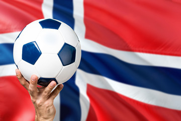 Norway soccer concept. National team player hand holding soccer ball with country flag background. Copy space for text.