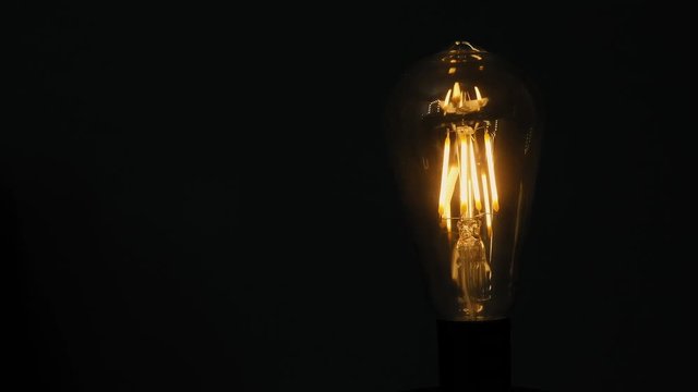 Classic edison light bulb close-up. Edison light bulb against the dark background. Vintage lamp light. Slow-motion zoom in