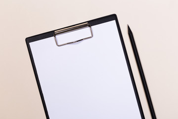 Clipboard with a white sheet and pen on a light background. View from above. space for text