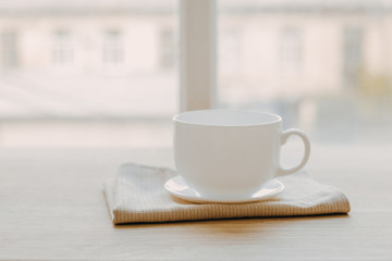 Wooden table with a towel and a white mug on a saucer on a blurred white background of modern kitchen