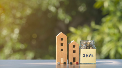 Wooden houses  model ,cars miniature and bottle of coins on table with natural background, loan or saving money for buy car or a house and real estate business investment concept