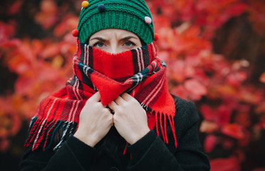 A young serious girl with her eyebrows shifted in a green knitted hat and a scarf covering her face...