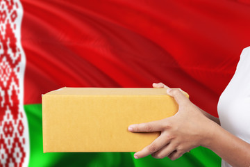 Belarus delivery service. International shipment theme. Woman courier hand holding brown box isolated on national flag background.