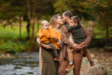 Happy young family with two sons on a walk in the autumn in the forest by the river.