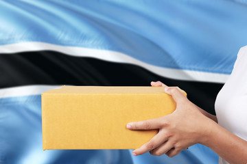 Botswana delivery service. International shipment theme. Woman courier hand holding brown box isolated on national flag background.