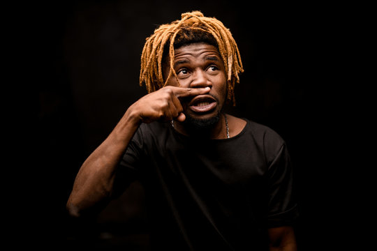 Black man with blonde dreadlocks posing in the dark outfit with the emotional face in action
