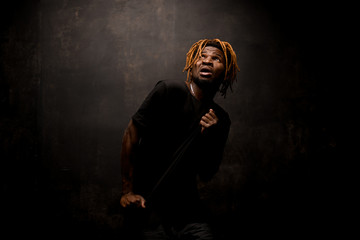 Black man with blonde dreadlocks posing in the dark outfit with the emotional face in action