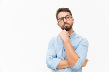 Pensive male customer looking away at copy space, touching chin, thinking. Handsome young man in casual shirt and glasses standing isolated over white background. Advertising concept