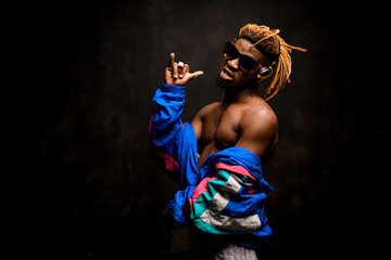 Black man with blonde dreadlocks posing in the colorful jacket, sunglasses and earphones with an...