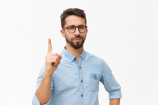 Positive Friendly Guy Having Idea And Pointing Index Finger Up. Handsome Young Man In Casual Shirt And Glasses Standing Isolated Over White Background. Advertising Concept