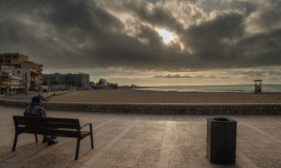 Fototapeta na wymiar Early morning on the embankment of the Mediterranean Sea man admires the dawn sitting on a bench