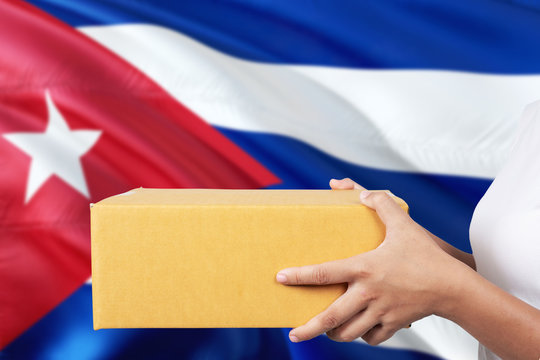 Cuba delivery service. International shipment theme. Woman courier hand holding brown box isolated on national flag background.