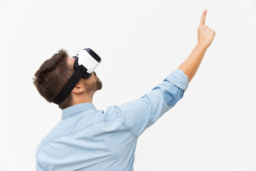 Bearded guy wearing VR goggles, pointing finger up. Young man in virtual reality headset standing isolated over white background. VR technology or advertising concept