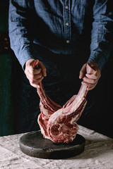 Man's hands holding raw uncooked black angus beef tomahawk steaks on bones on linen table cloth....