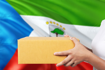 Equatorial Guinea delivery service. International shipment theme. Woman courier hand holding brown box isolated on national flag background.