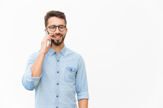 Positive Guy Talking On Cellphone, Enjoying Nice Conversation. Handsome Young Man In Casual Shirt And Glasses Standing Isolated Over White Background. Phone Call Concept