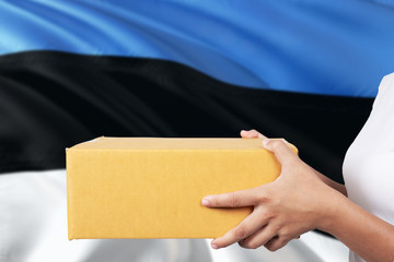 Estonia delivery service. International shipment theme. Woman courier hand holding brown box isolated on national flag background.