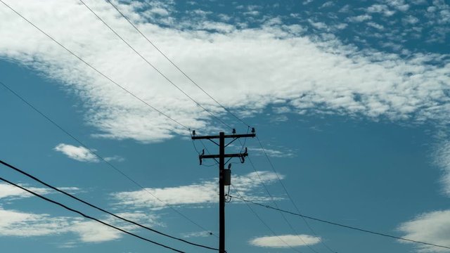 Timelapse, white clouds drift by electric power pole and wires in blue sky