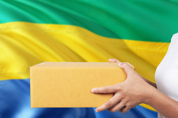 Gabon delivery service. International shipment theme. Woman courier hand holding brown box isolated...