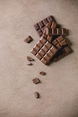 Dark and milk chocolate bar whole and chopped over brown texture background. Flat lay, space