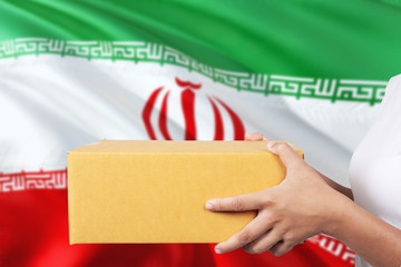 Iran delivery service. International shipment theme. Woman courier hand holding brown box isolated on national flag background.