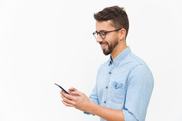 Joyful guy texting message on smartphone. Handsome young man in casual shirt and glasses standing isolated over white background. Cellphone using concept
