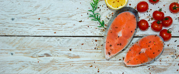 Cooking concept. Fresh salmon steaks with lemon, spices and cherry tomatoes on a light wooden background.