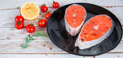 Cooking concept. Fresh salmon steaks with lemon, spices and cherry tomatoes on a light wooden background.