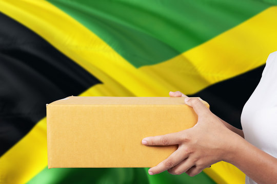 Jamaica delivery service. International shipment theme. Woman courier hand holding brown box isolated on national flag background.