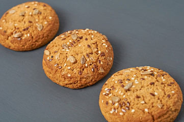 Row of three fresh homemade cookies with seeds of sunflower and sesame lies on dark scratched concrete table on kitchen. Close-up