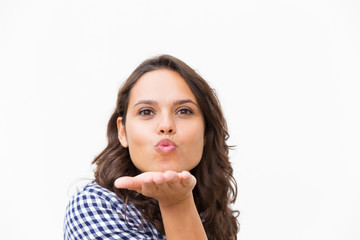 Cute cheerful Latin woman blowing kiss, expressing love or tenderness. Young woman in casual checked shirt standing isolated over white background. Air kiss concept